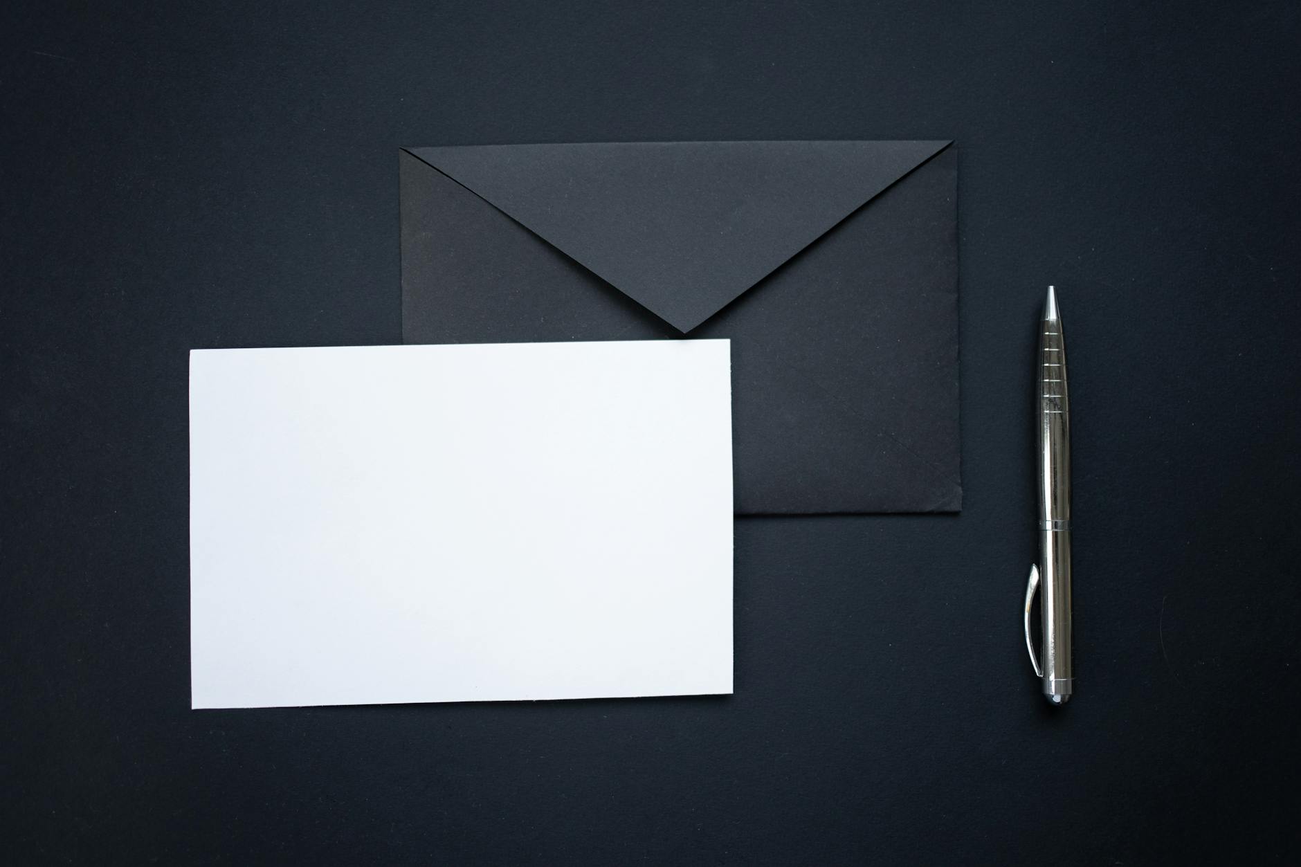 a piece of blank paper on a black envelope beside a silver ball pen